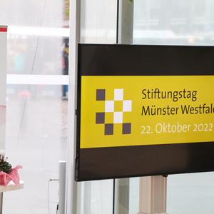 Informationsschild zum Stiftungs­tag Münster Westfalen am 22. Oktober 2022, neben einer Pflanze auf einem Tisch.