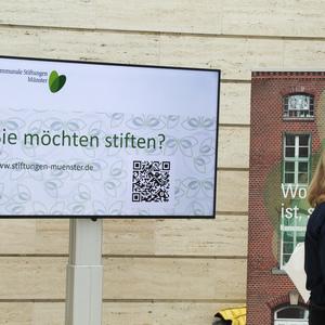Informationsdisplay der Kommunalen Stiftungen Münster mit der Frage „Sie möchten stiften?“ und QR-Code.