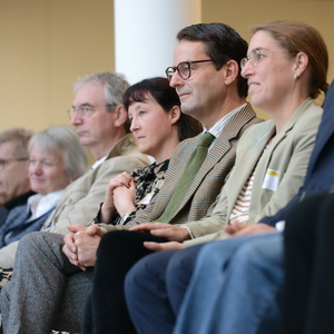 Gruppe von Personen sitzt nebeneinander in einer Veranstaltung, aufmerksam auf das Geschehen vor ihnen blickend.