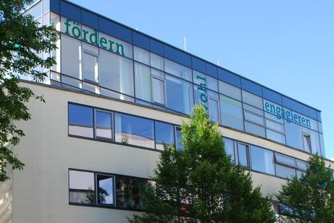 Moderne Architektur eines Bürogebäudes mit großen Fenstern und grünen Beschriftungen an der Fassade, umgeben von Bäumen.