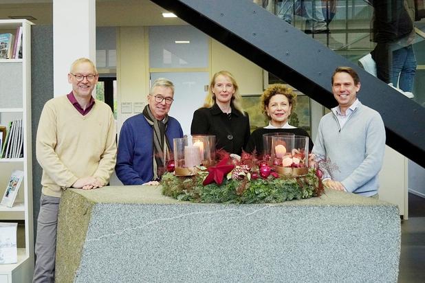 Fünf Personen stehen an einem dekorierten Empfangstresen mit Kerzen und Weihnachtskranz in einem modernen Innenraum.
