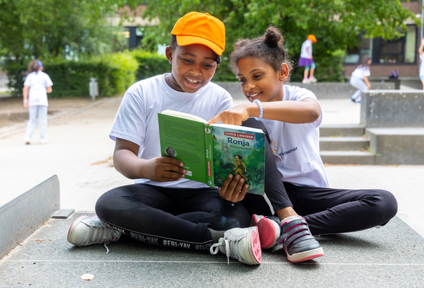 Zwei Kinder sitzen auf einer Bank und lesen gemeinsam das Buch „Ronja Räubertochter“.