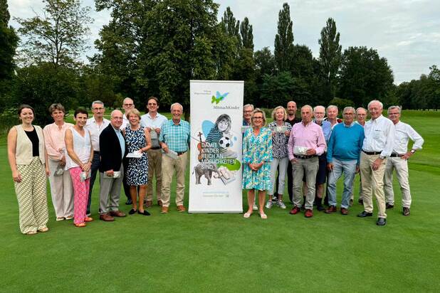 Gruppe von 18 Personen auf einem Golfplatz, posierend vor einem Banner mit dem Motto „Für Kinder und Möglichkeiten“.