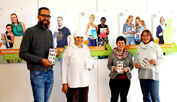 Vier Personen halten Informationsmaterial in der Hand, vor ihnen hängen Plakate zu ehrenamtlicher Unterstützung.