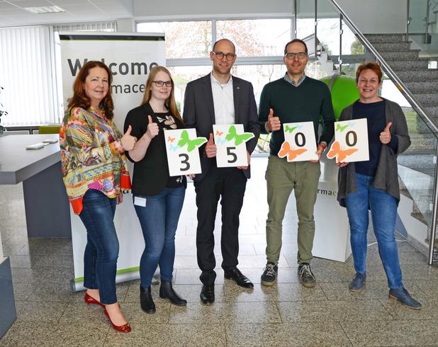 Fünf Personen zeigen mit Daumen nach oben Zahlenkarten mit den Werten 3, 5 und 0 in einer modernen Büroumgebung.