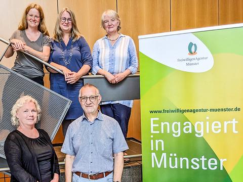 F&uuml;nf Personen stehen und sitzen um einen Tisch mit Informationsmaterialien zur Freiwilligenagentur M&uuml;nster.